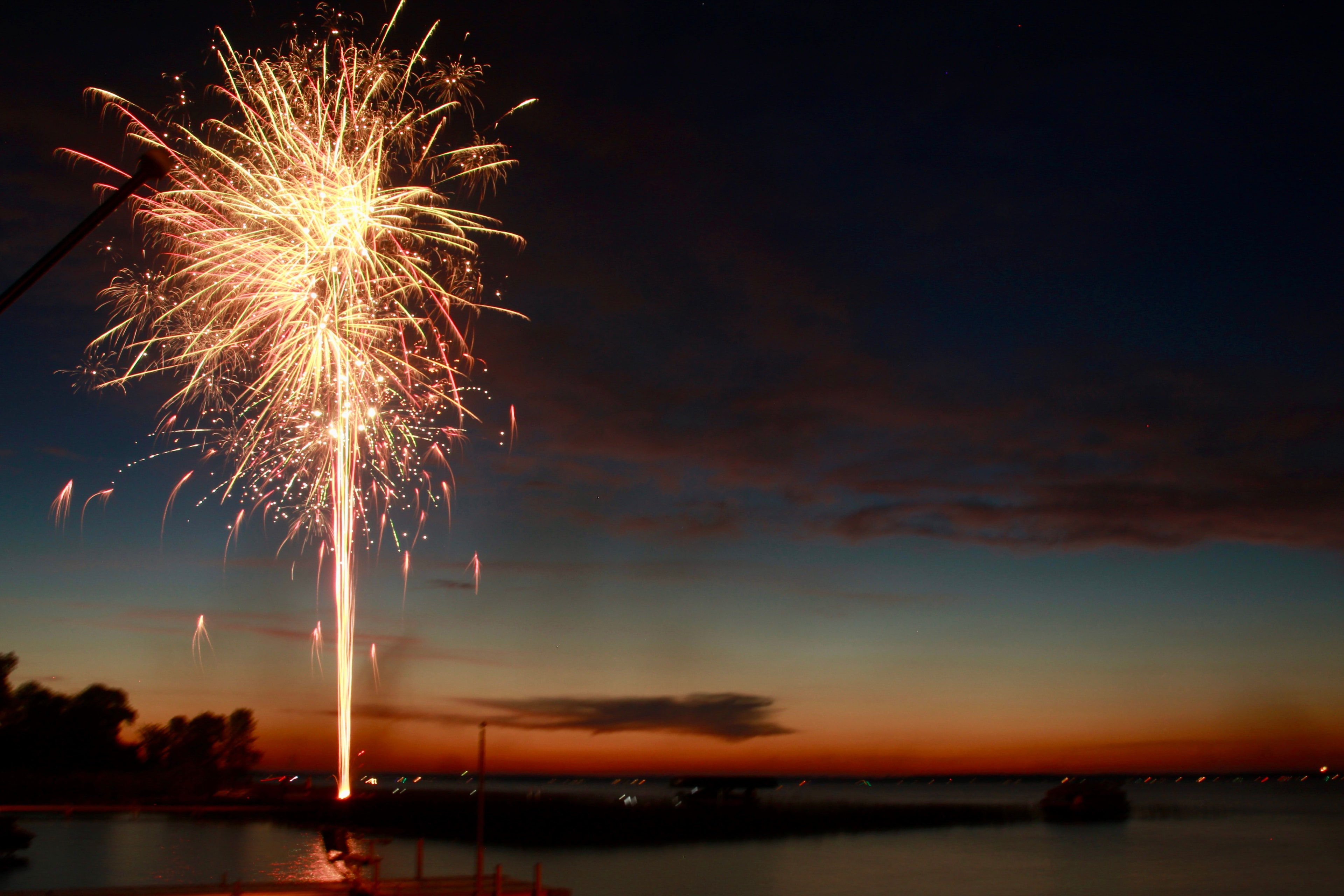 Fireworks bursting over water at dusk, long exposure